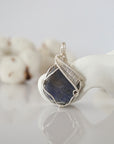 Front view of raw sapphire pendant — natural unpolished dark blue corundum stone hand-wrapped in detailed silver finish wire, handcrafted artisan crystal jewelry