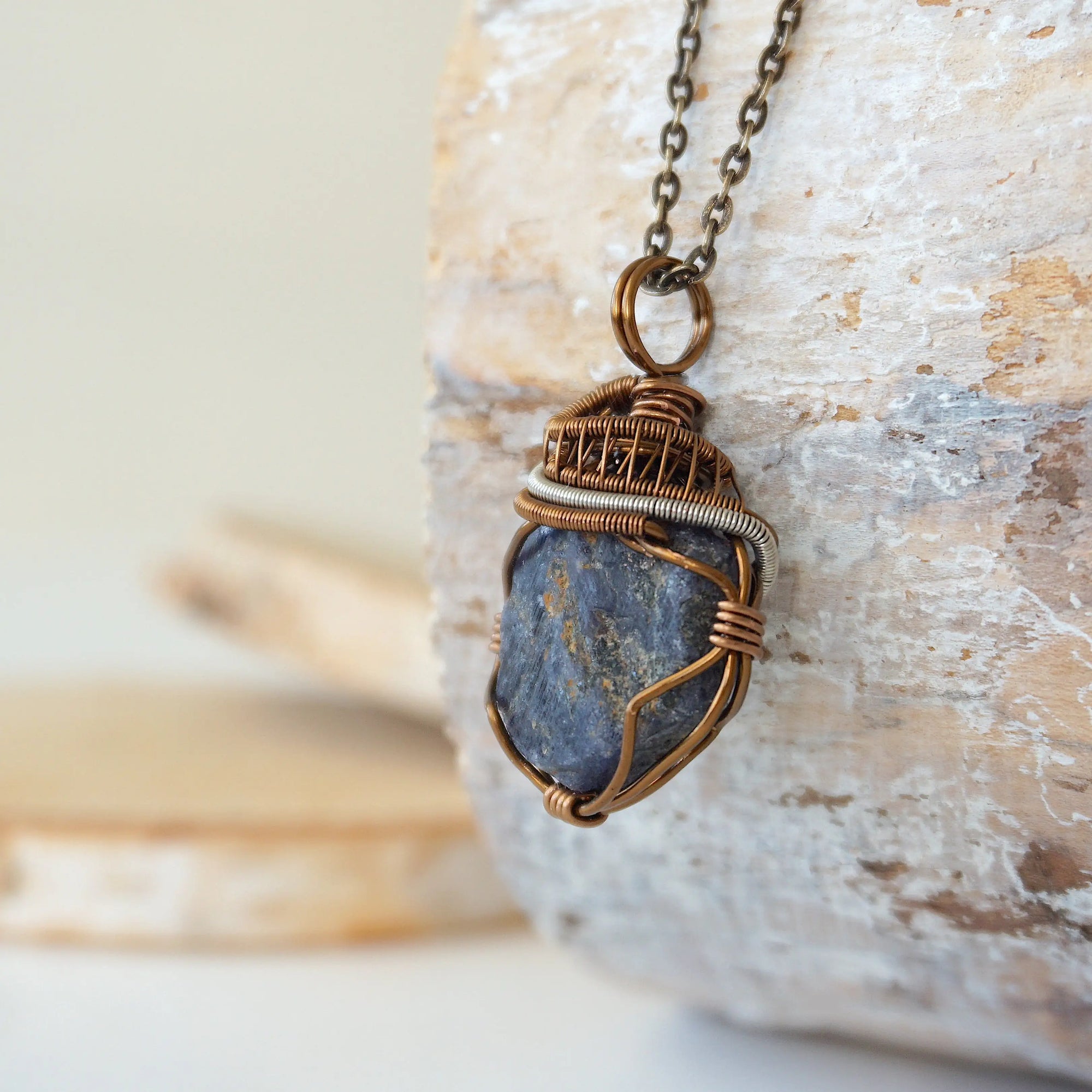 Left-angle close-up of raw sapphire pendant revealing the dual-metal wire-wrapping craftsmanship in antique bronze and dark silver
