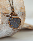 Right-angle detail of raw sapphire pendant showing artisan wire-wrapping in antique bronze and dark silver — handcrafted crystal necklace