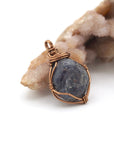 Right-angle detail of raw sapphire pendant showing artisan wire-wrapping technique in antique bronze — handcrafted crystal jewelry