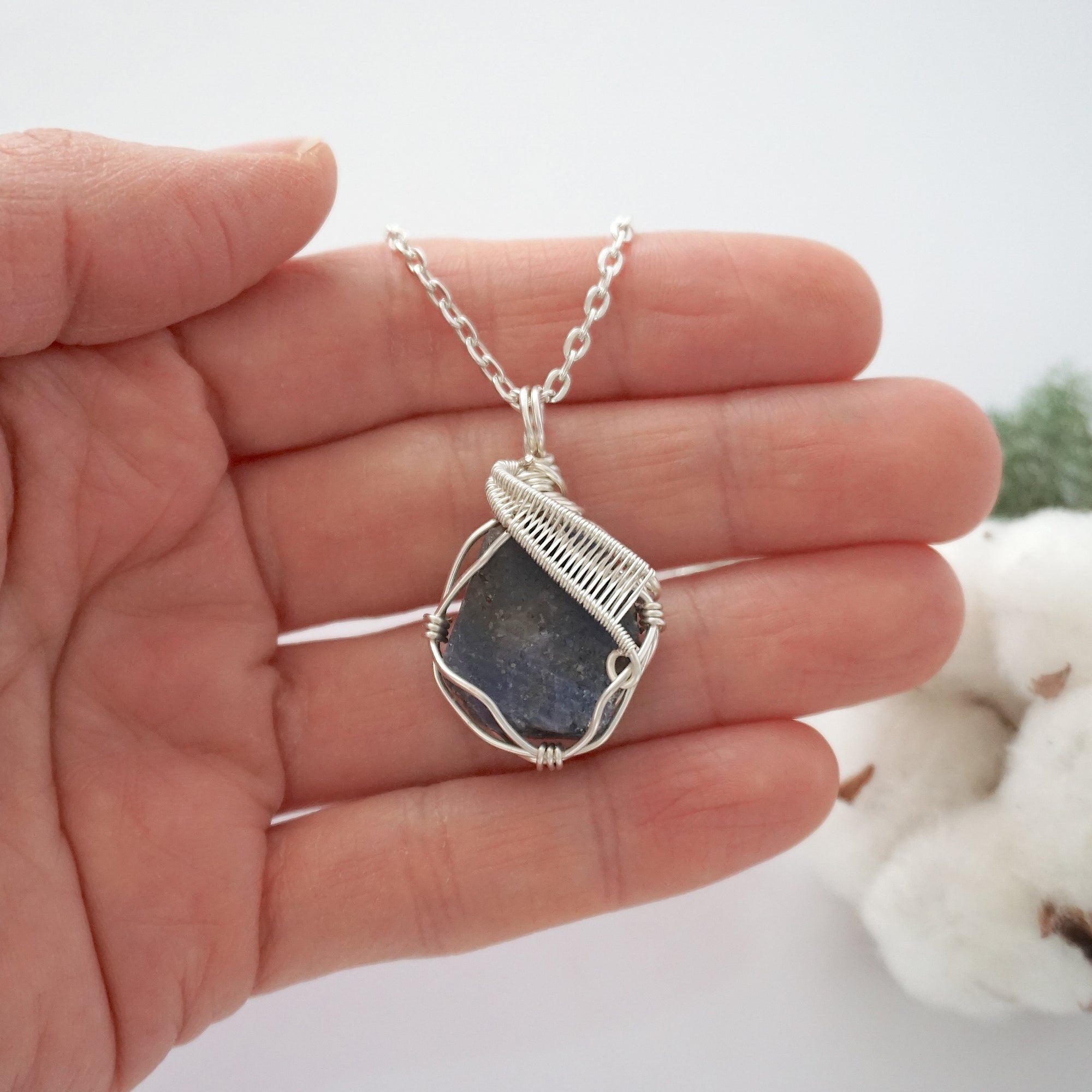 Handmade raw sapphire pendant held in hand showing size — natural dark blue sapphire stone wire wrapped in silver finish, 25-30 carats, statement piece, one of a kind