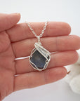 Handmade raw sapphire pendant held in hand showing size — natural dark blue sapphire stone wire wrapped in silver finish, 25-30 carats, statement piece, one of a kind