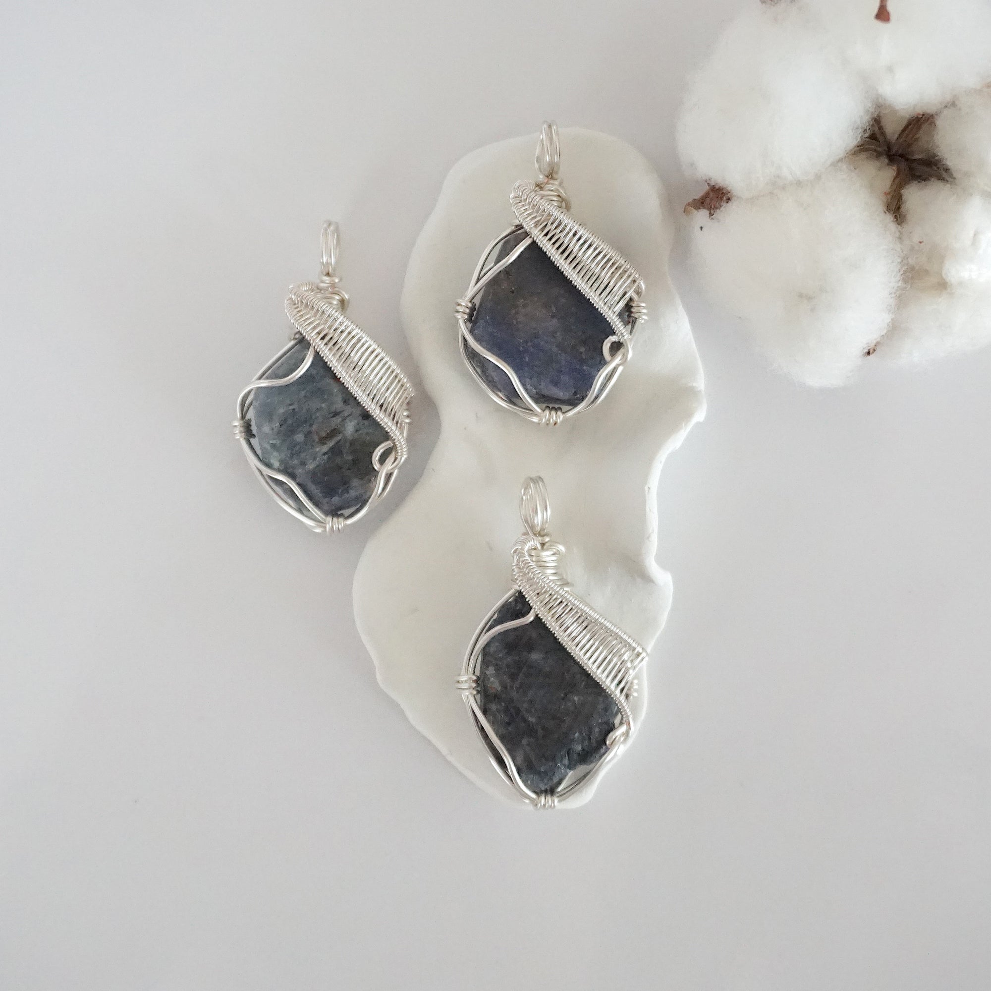 Three raw sapphire pendants showing natural variation in stone size, shape, and blue-grey tone — each one of a kind, September birthstone, silver wire wrapped, Designs by Nature Gems
