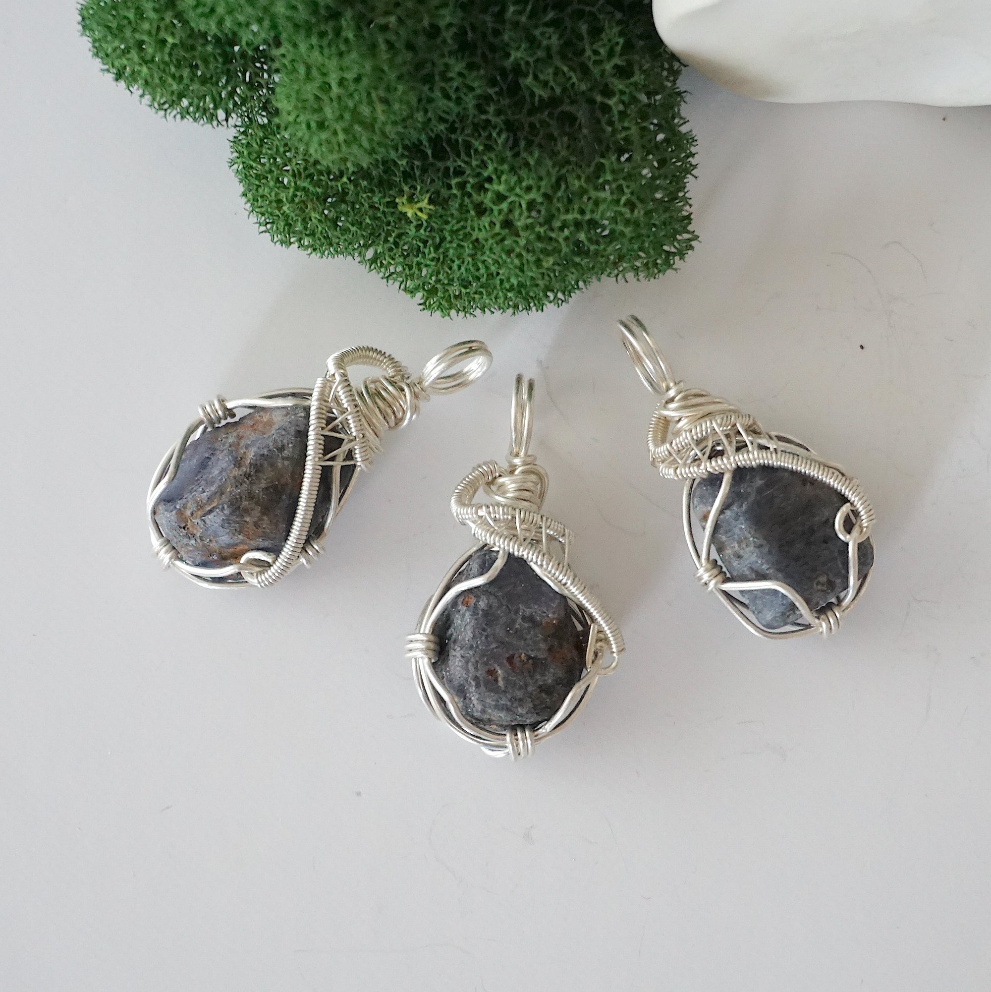 Three raw sapphire pendants showing natural variation in stone size, shape, and blue-grey tone — each one of a kind, September birthstone, 925 sterling silver wire wrapped, Designs by Nature Gems