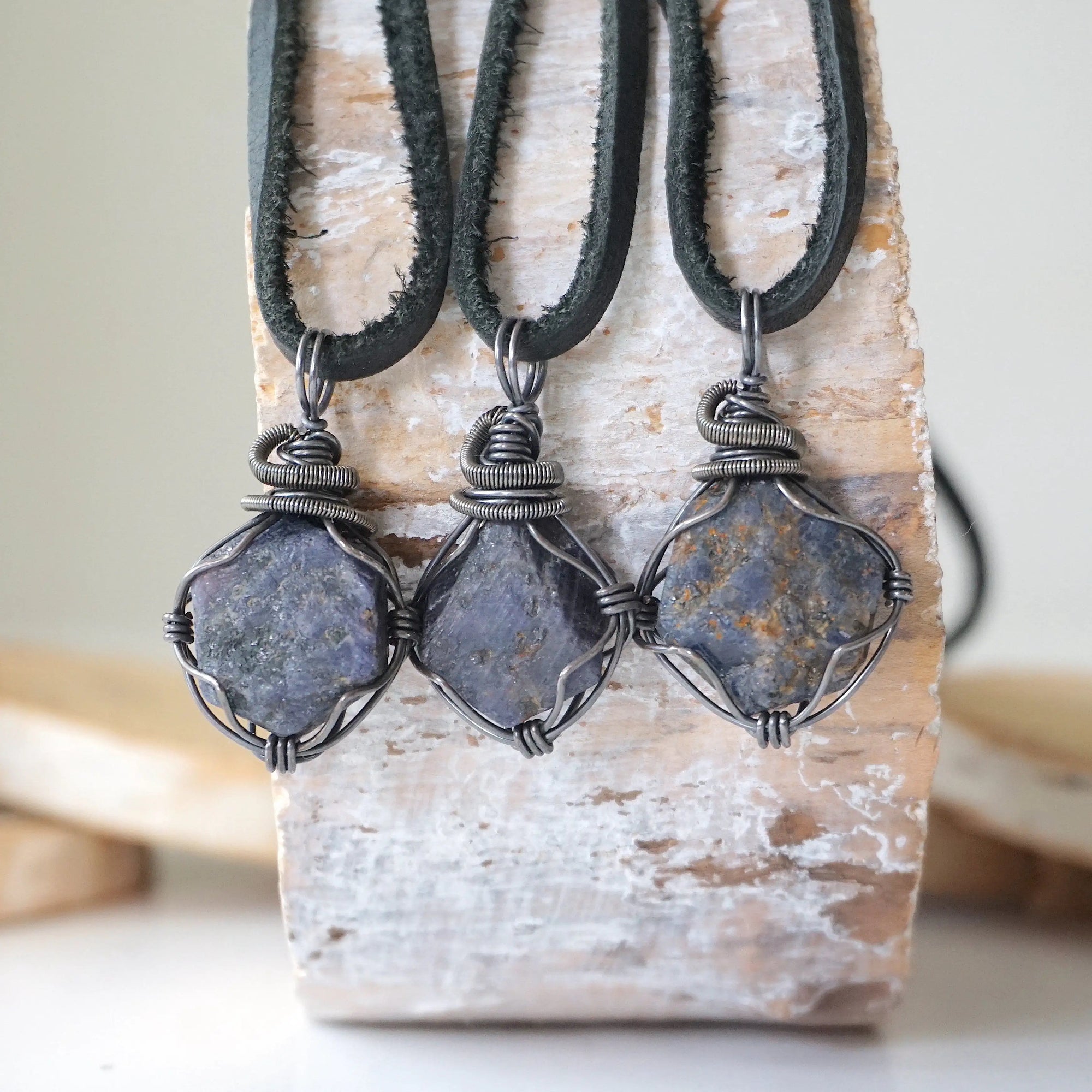 Three raw sapphire pendants showing natural variation in size, shape, and depth of colour — each men's antiqued sterling silver wire-wrapped necklace is individually handcrafted and one of a kind