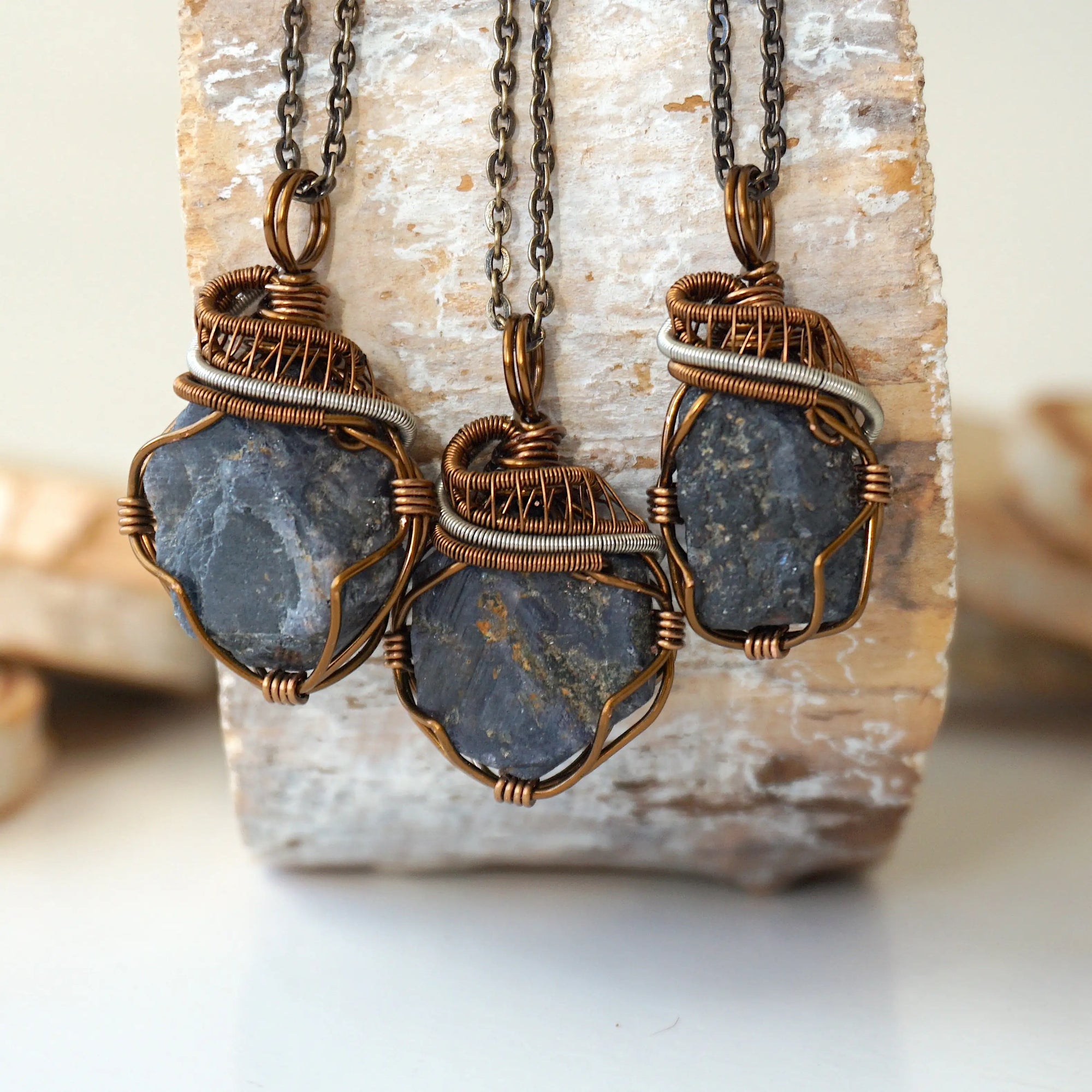 Three raw sapphire pendants showing natural variation in size, shape, and depth of colour — each wire-wrapped antique bronze and dark silver necklace is individually handcrafted and one of a kind