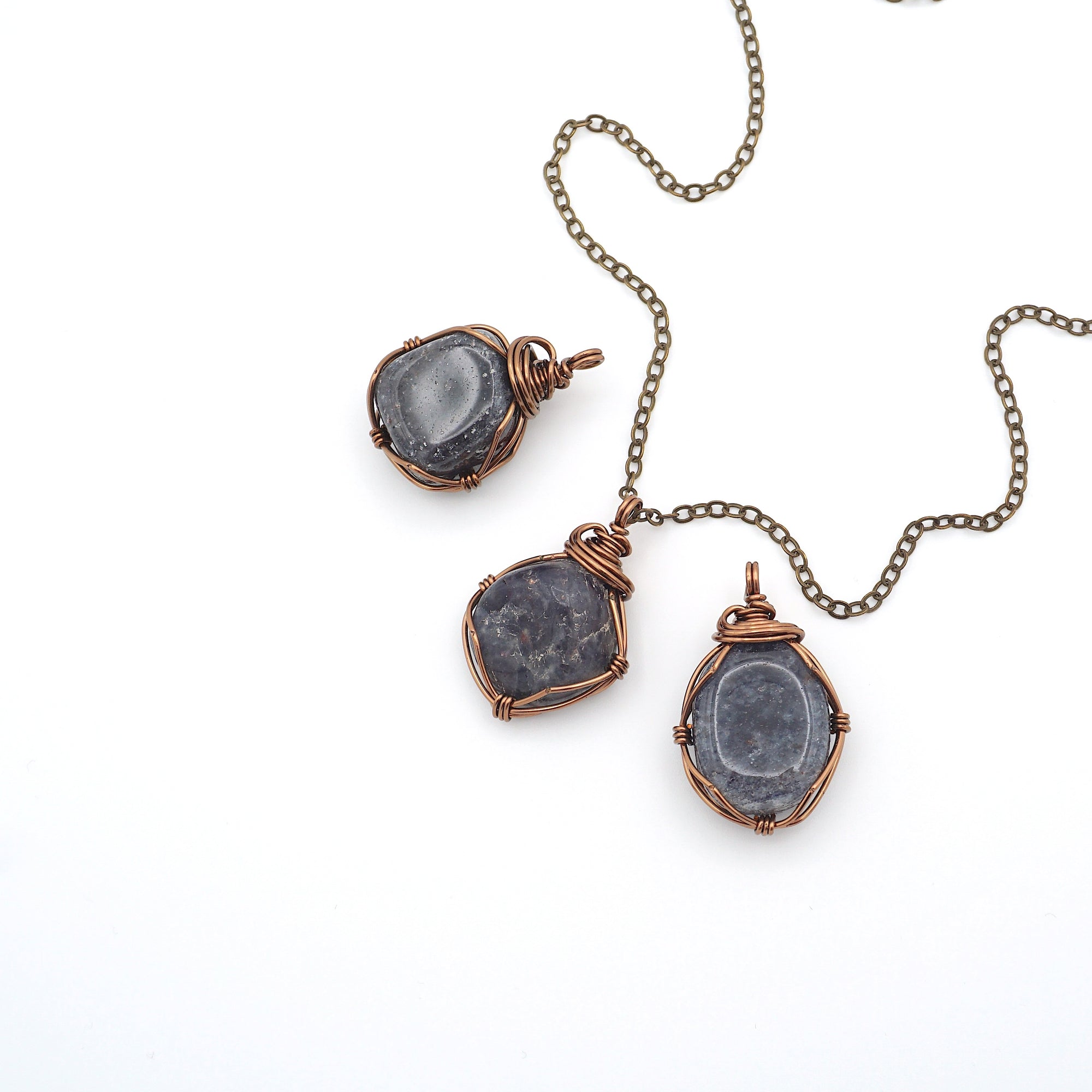 Three raw sapphire pendants showing natural variation in size, shape, and depth of colour — each wire-wrapped antique bronze necklace is one of a kind