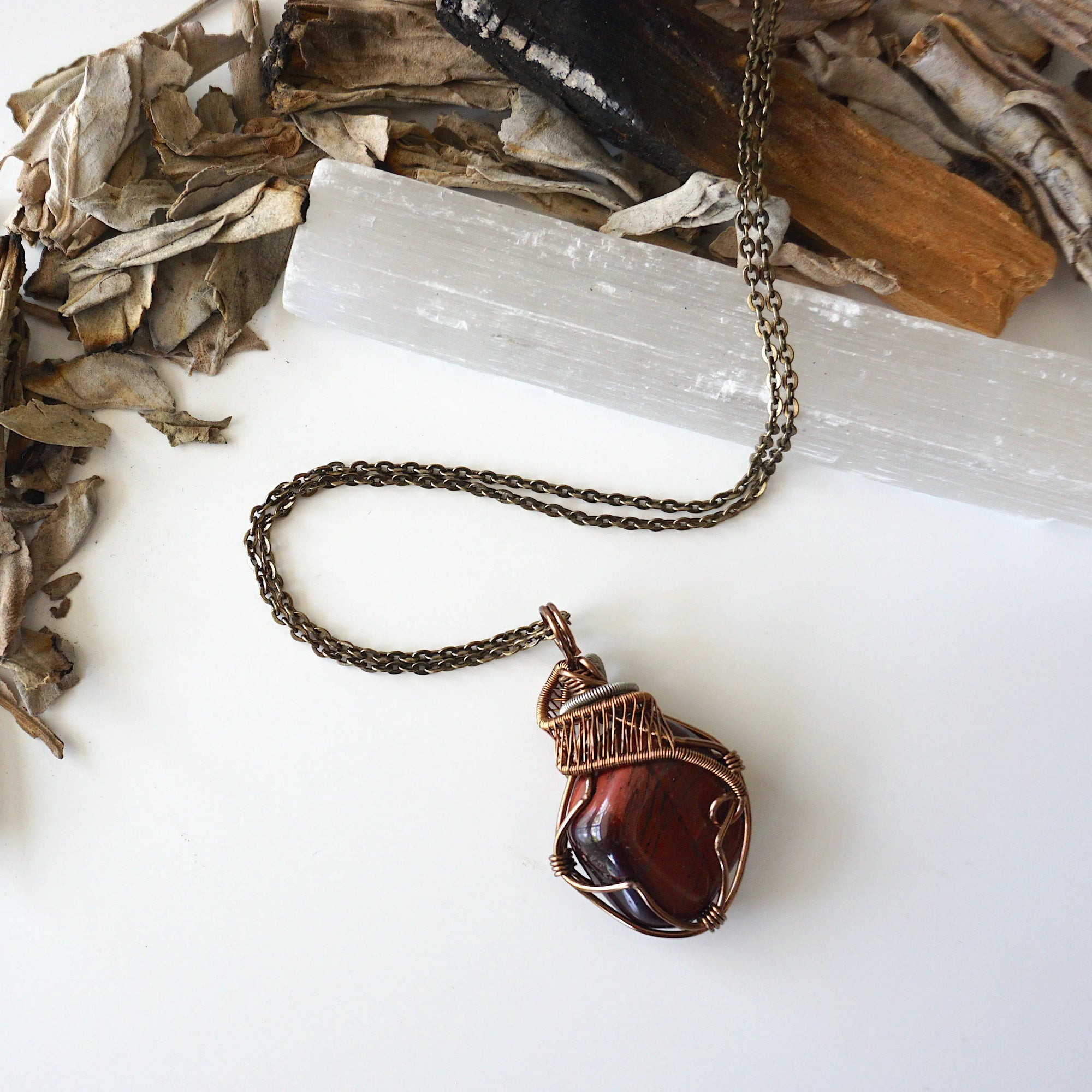 Natural red tiger's eye pendant on antique bronze chain, laying flat, artisan jewelry by Designs by Nature Gems.