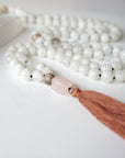 Close-up of rose quartz guru bead and long brown tassel on rainbow moonstone mala necklace, traditional knotted silk cord finish.