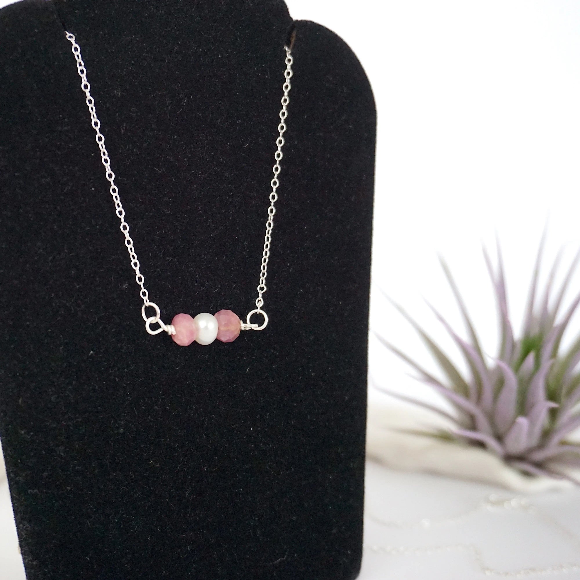 Focused left-side close-up of sterling silver ruby and pearl bar necklace on jewelry display