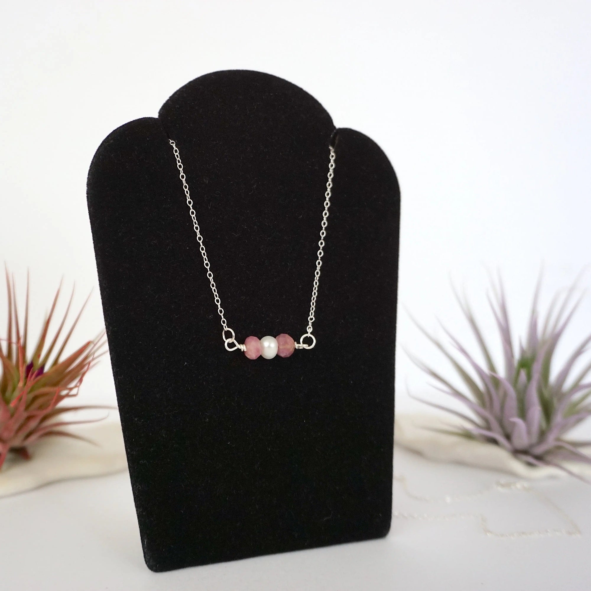 Right angle view of ruby and freshwater pearl bar necklace in 925 sterling silver on jewelry display