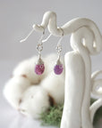 Side view of ruby sterling silver drop earrings showing wire wrapped natural faceted ruby, artisan craftsmanship, on a display – Designs by Nature Gems