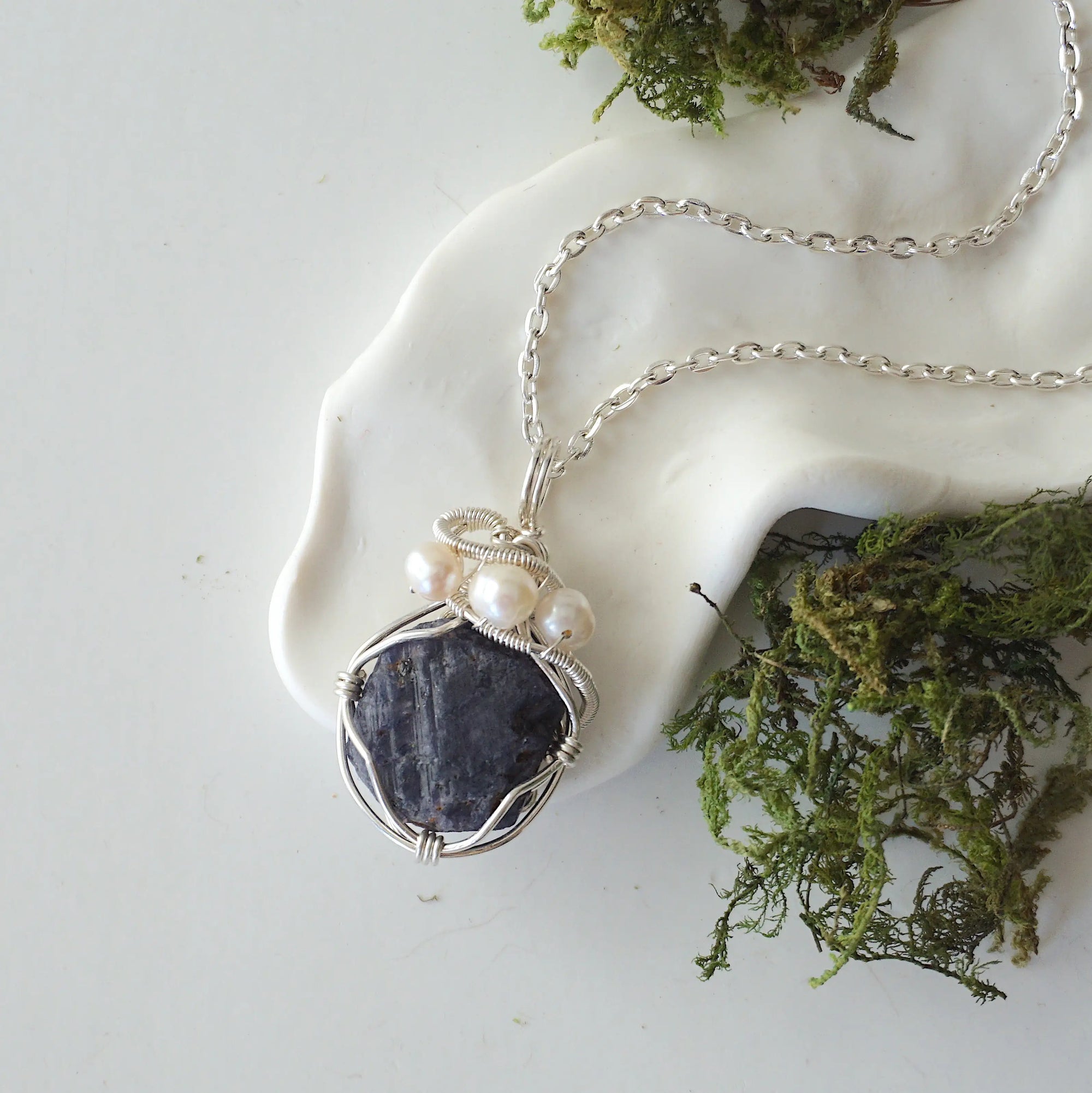 Handmade silver wire wrapped sapphire and freshwater pearl necklace laying flat on a silver plated chain, artisan jewelry for women