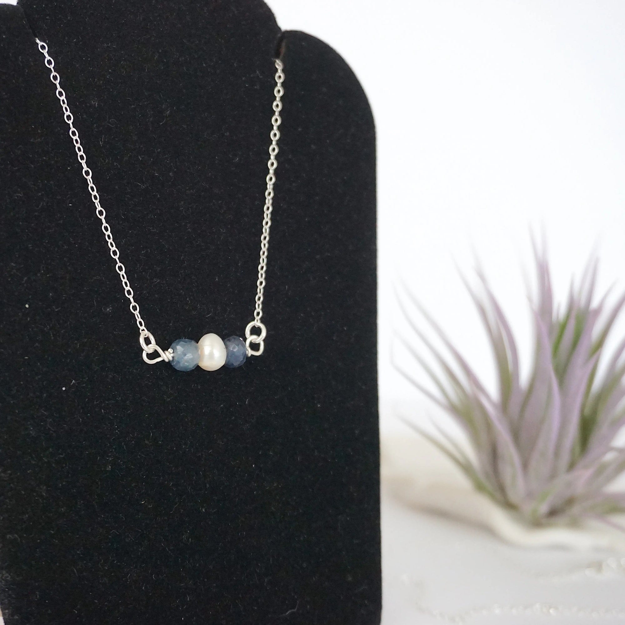 Focused left-side close-up of sterling silver sapphire and pearl bar necklace on jewelry display