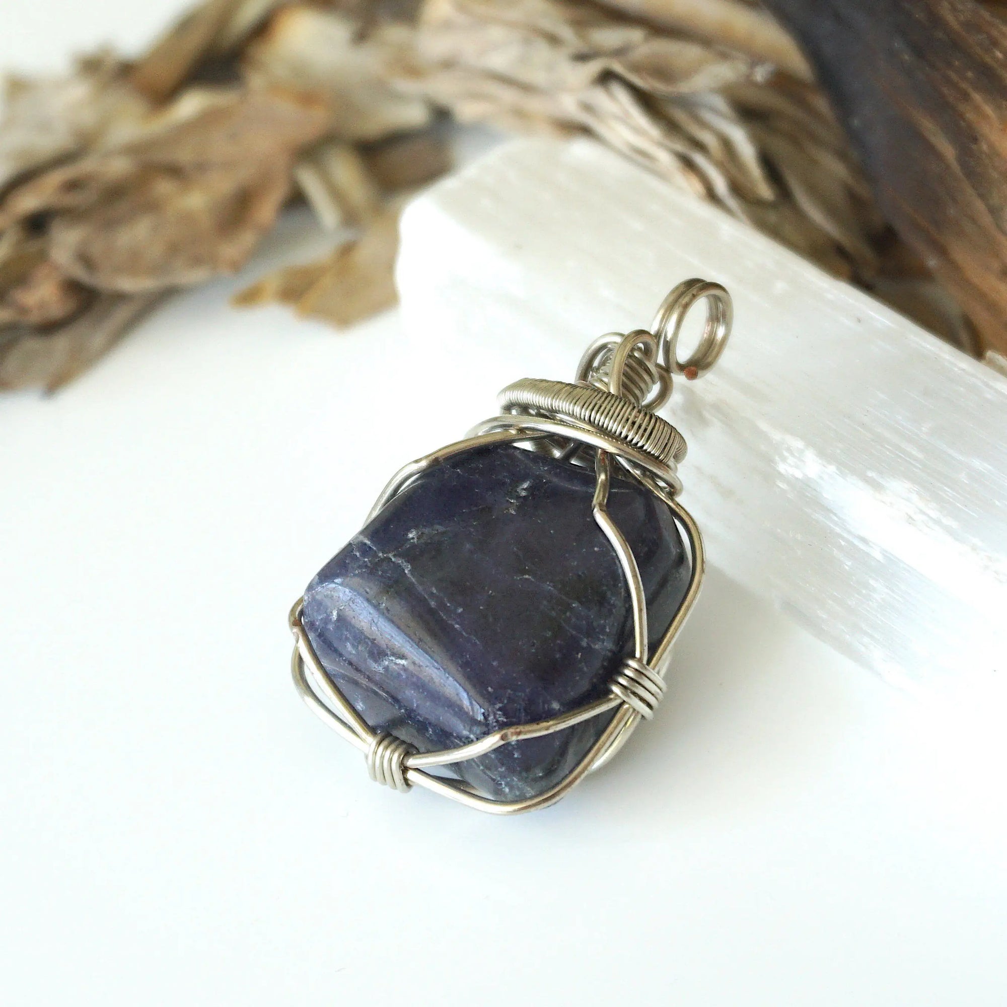 Left-angle close-up of sapphire pendant revealing the precision of dark silver wire-wrapping craftsmanship — artisan crystal jewelry