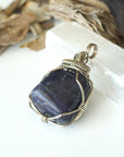 Left-angle close-up of sapphire pendant revealing the precision of dark silver wire-wrapping craftsmanship — artisan crystal jewelry
