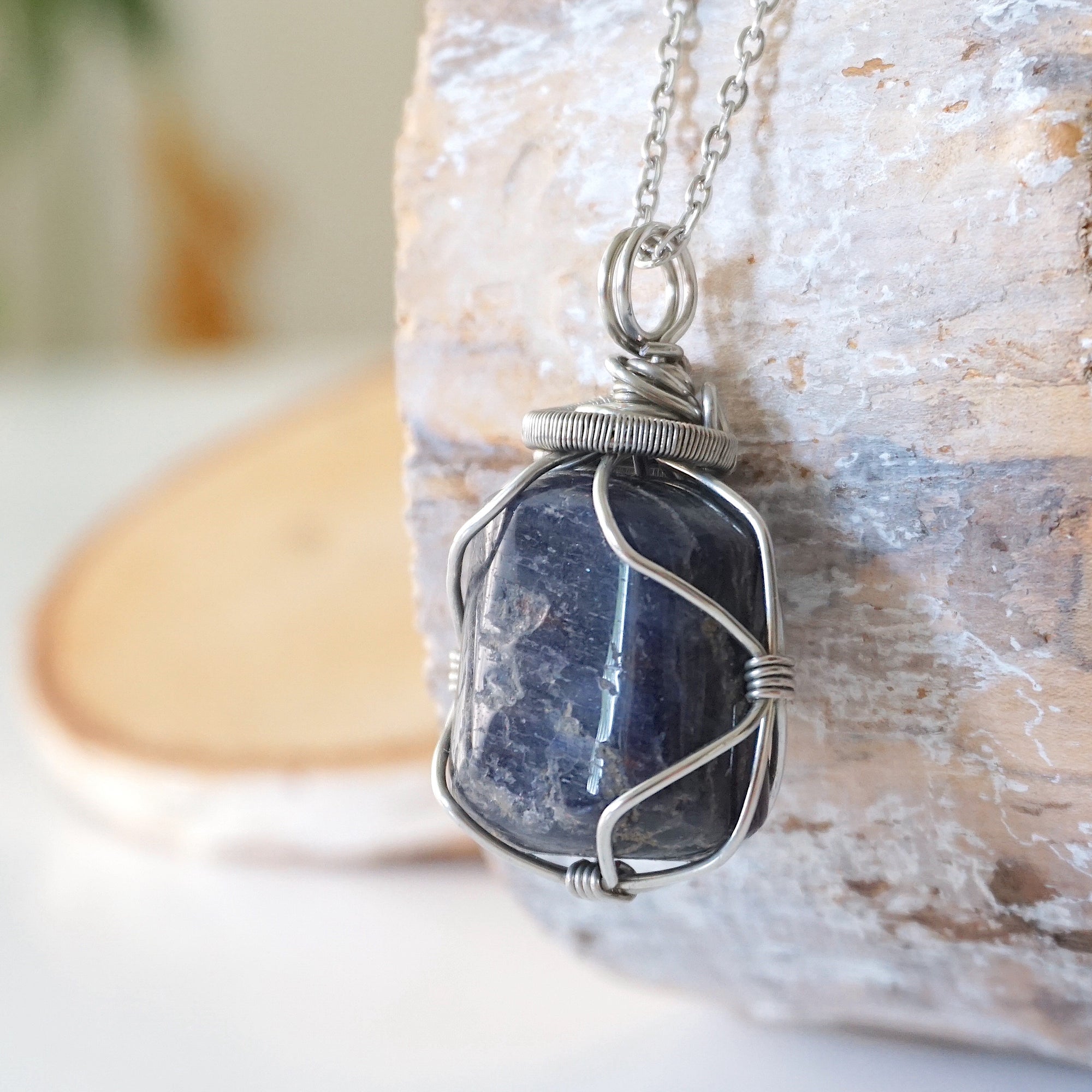 Left-angle close-up of sapphire pendant revealing the precision of dark silver wire-wrapping craftsmanship — white gold plated chain, artisan crystal jewelry