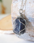 Left-angle close-up of sapphire pendant revealing the precision of dark silver wire-wrapping craftsmanship — white gold plated chain, artisan crystal jewelry
