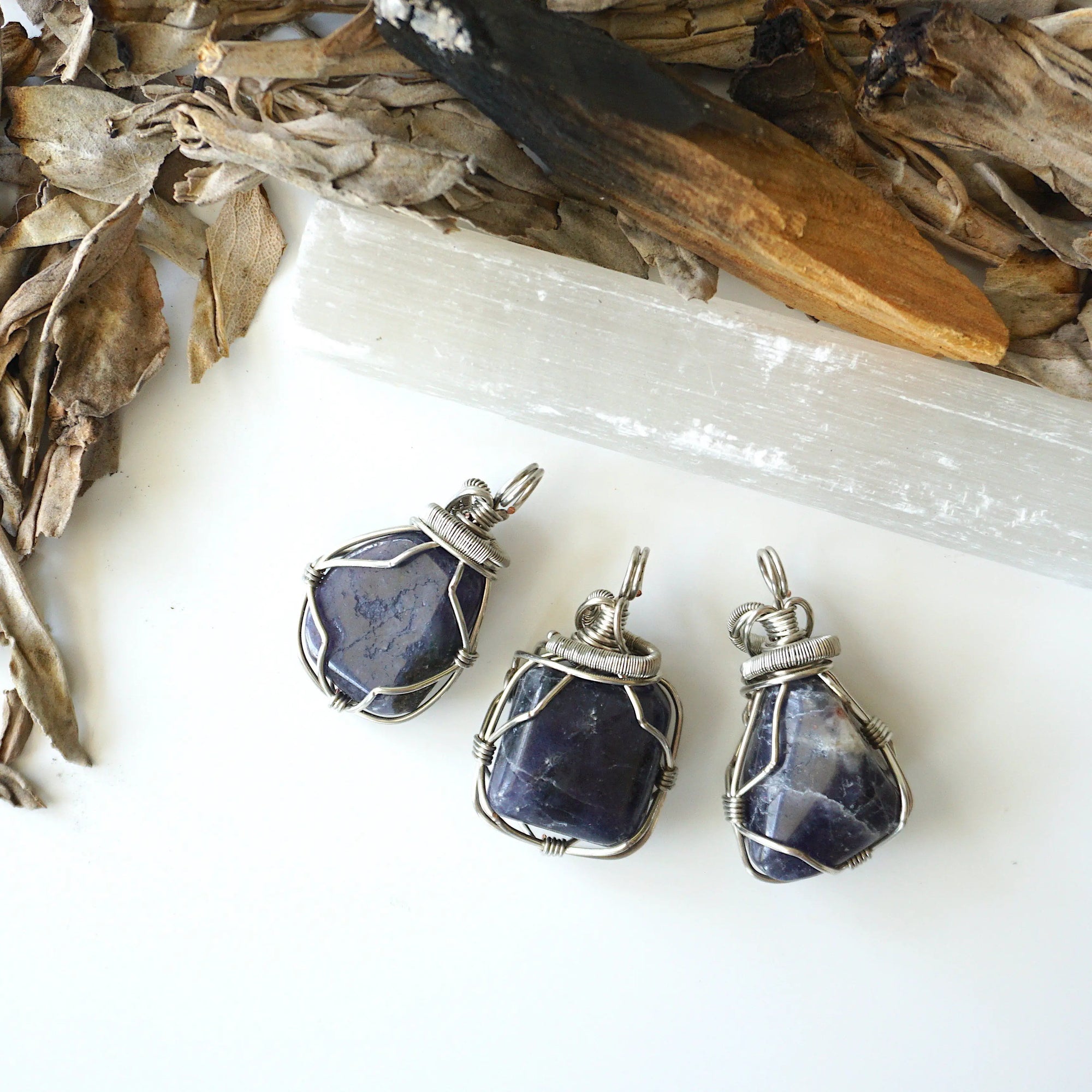 Three natural sapphire pendants showing variation in size, shape, and depth of colour — each dark silver wire-wrapped necklace is individually handcrafted and one of a kind