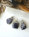 Three natural sapphire pendants showing variation in size, shape, and depth of colour — each dark silver wire-wrapped necklace is individually handcrafted and one of a kind