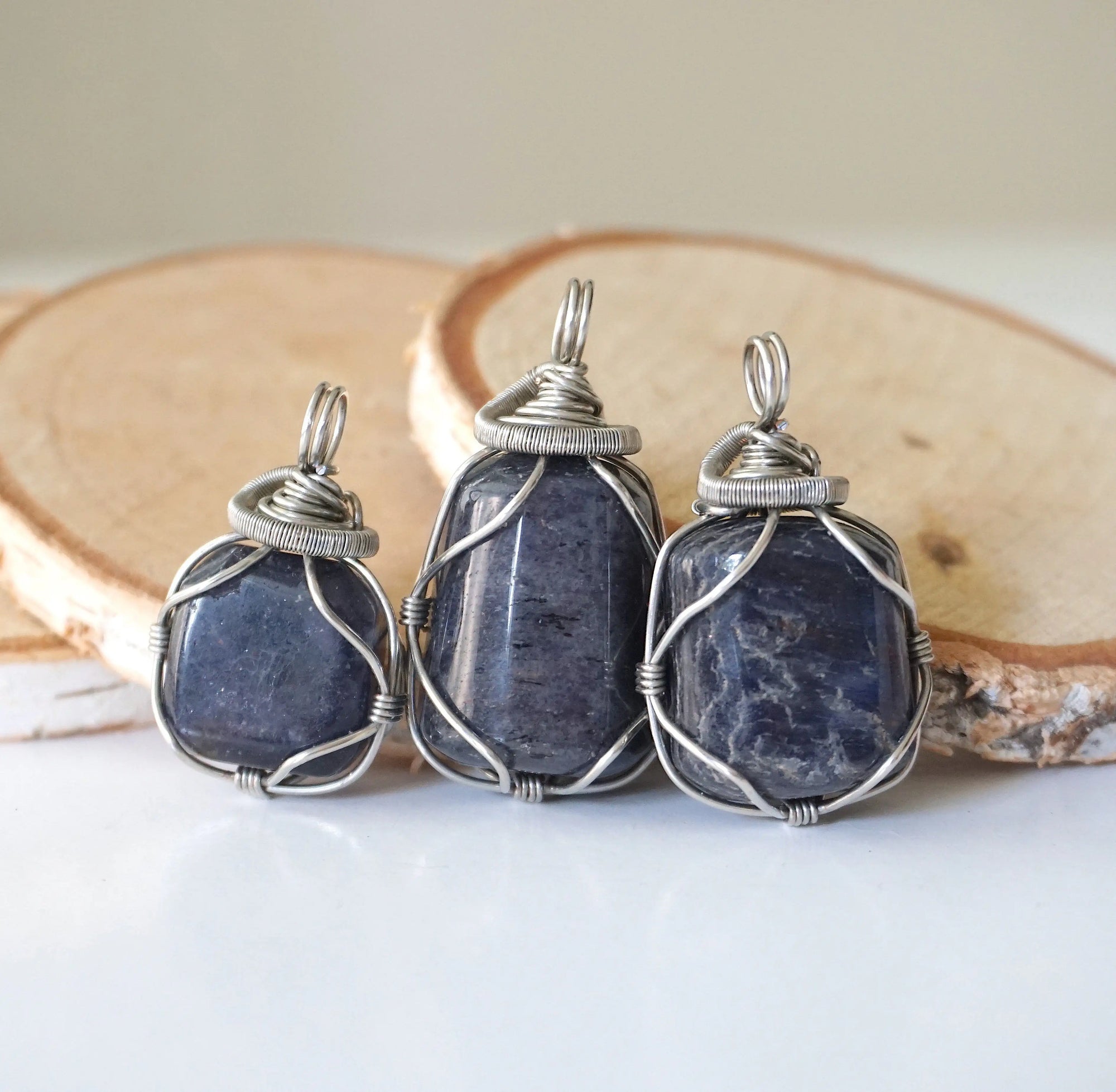 Three natural sapphire pendants showing variation in size, shape, and depth of colour — each dark silver wire-wrapped necklace is individually handcrafted and one of a kind