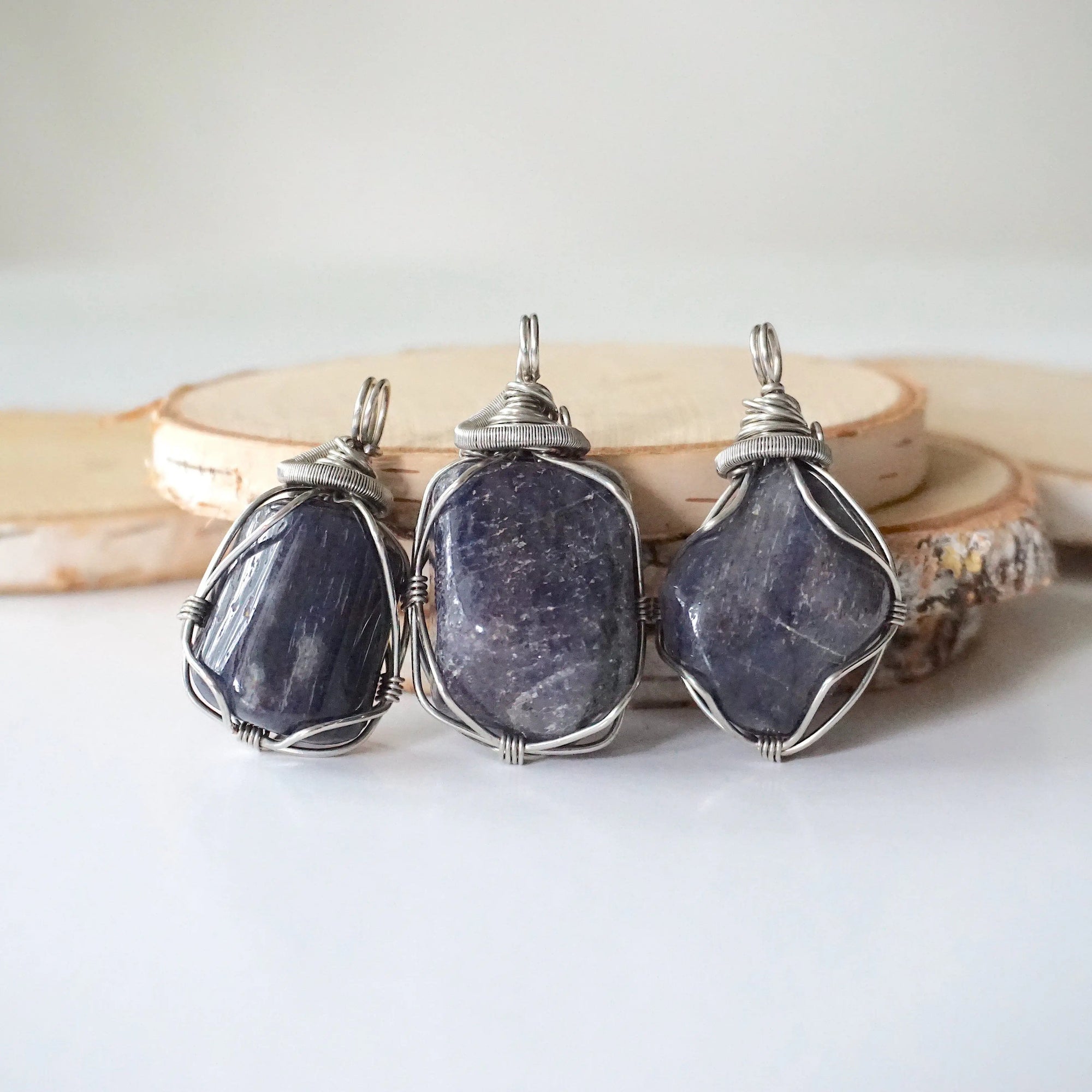Three natural sapphire pendants showing variation in size, shape, and depth of colour — each men's dark silver wire-wrapped necklace is individually handcrafted and one of a kind