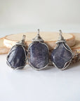 Three natural sapphire pendants showing variation in size, shape, and depth of colour — each men's dark silver wire-wrapped necklace is individually handcrafted and one of a kind