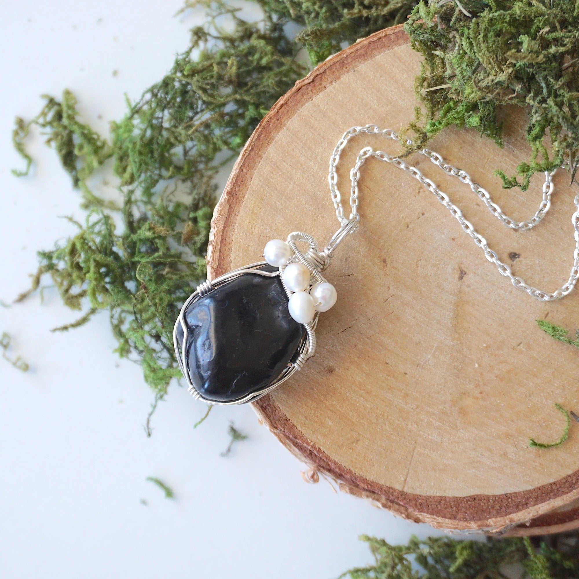 Handmade silver wire wrapped shungite and freshwater pearl necklace laying flat on a silver plated chain, artisan jewelry for women