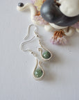 Emerald drop earrings on flat surface showing fish hook ear wire style and handcrafted wire wrapped emerald design