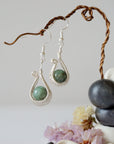 Close detail of wire wrapped emerald drop earrings showing intricate artisan wrapping around natural emerald bead