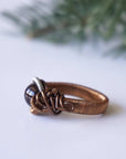 Left side angle view of a gender neutral wire wrapped garnet ring in antique bronze and tin-plated copper